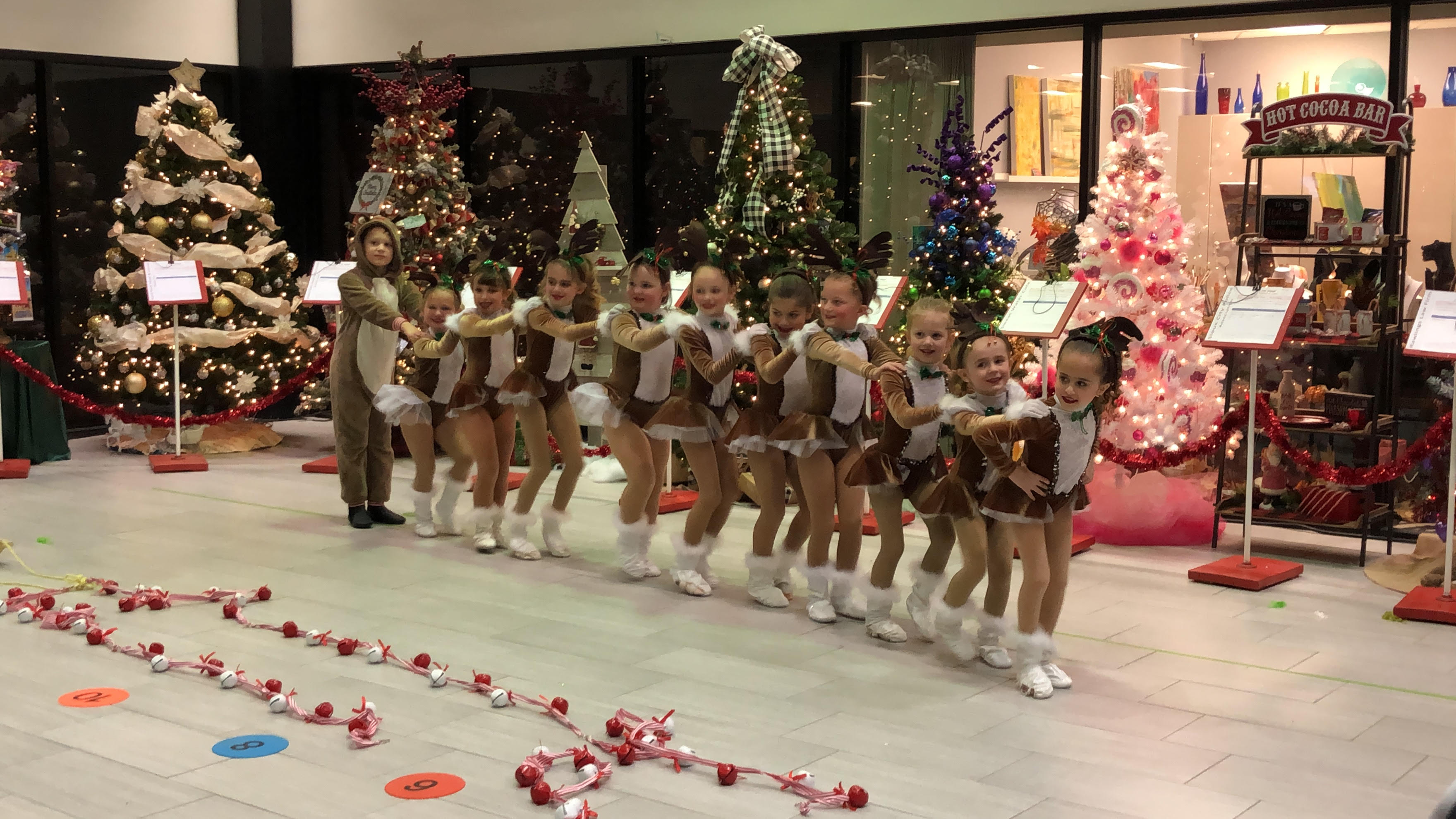 A long dance line of children in front of christmas trees